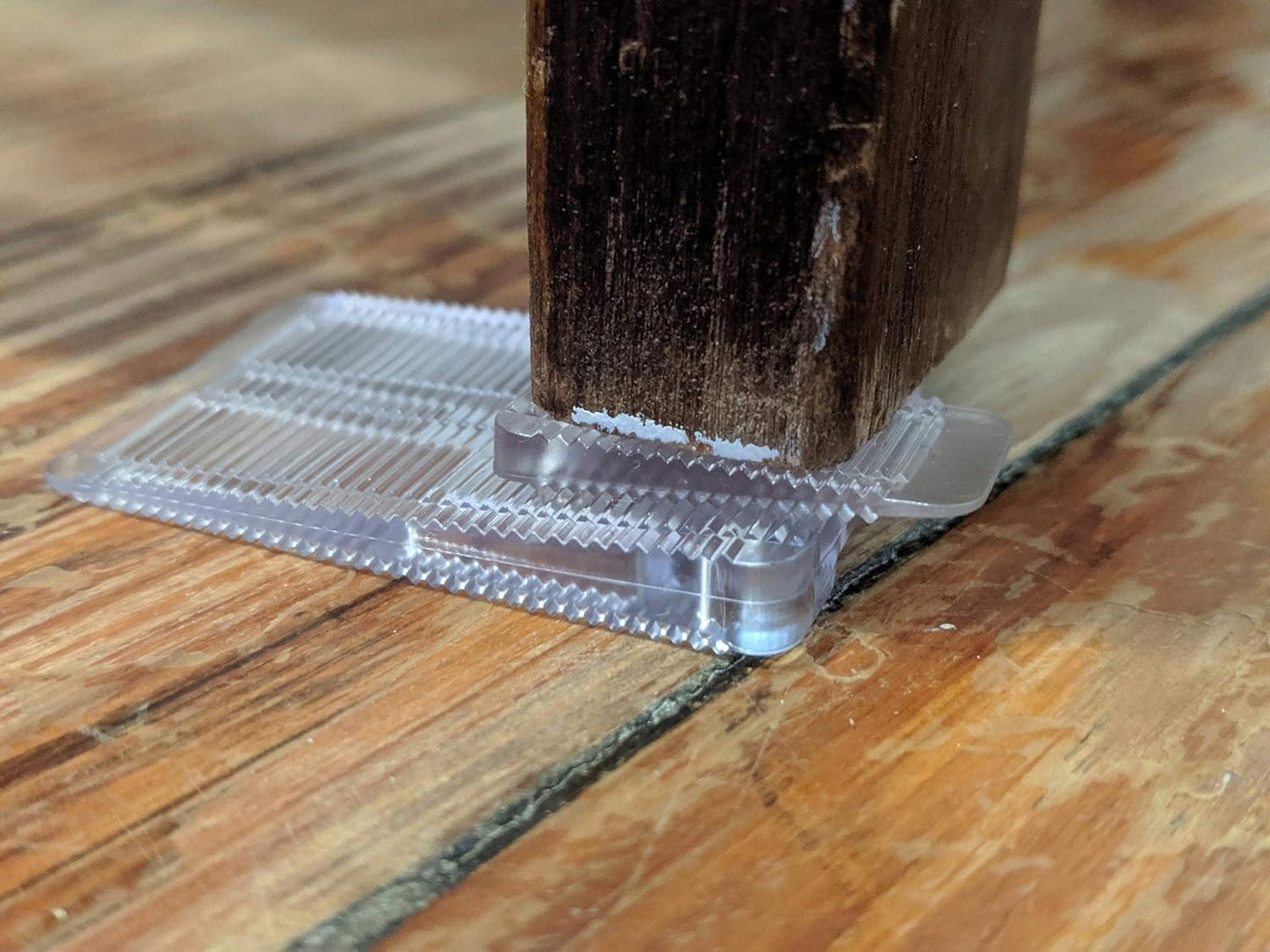 Stacked clear Wobble Wedges under a furniture leg on a wooden floor for stability
